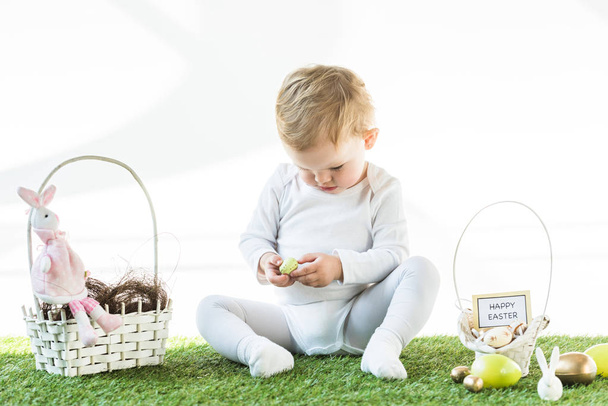 adorable enfant assis près de paniers de paille avec des œufs de Pâques, lapins décoratifs et carte de Pâques heureux isolé sur blanc
 - Photo, image