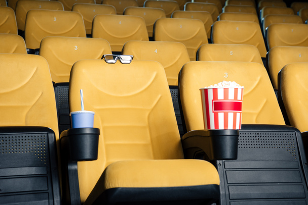Oranje bioscoopstoelen met papieren kopjes soda en popcorn in bekerhouders en 3D-bril - Foto, afbeelding
