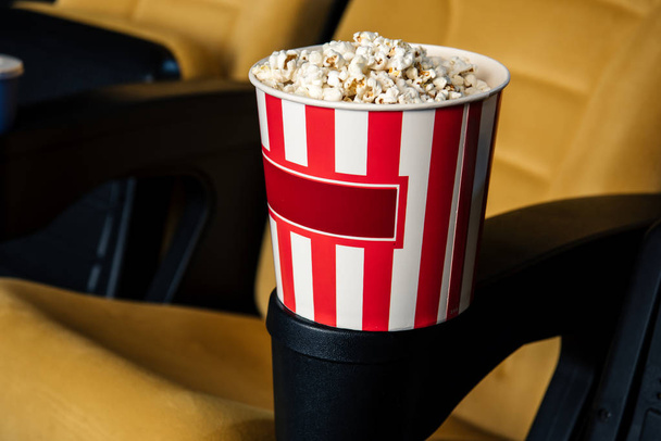selective focus of cinema seat with stripped paper cup of popcorn in cup holder - Photo, image