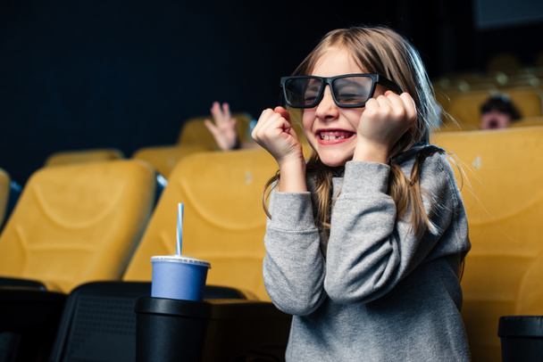 emotionele kind in 3d bril kijken naar film terwijl u zit in de buurt van papier beker - Foto, afbeelding
