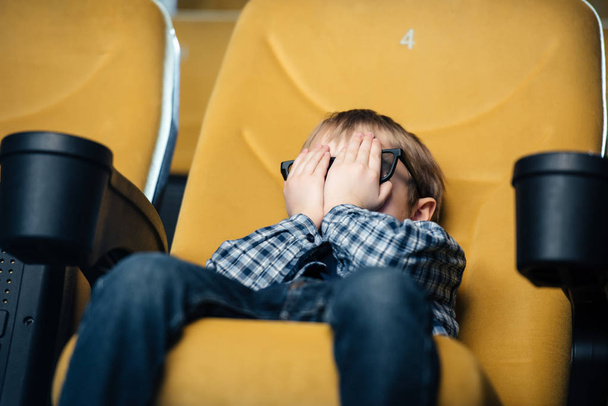 frightened boy holding hands on face while sitting in cinema and watching movie - Foto, Bild