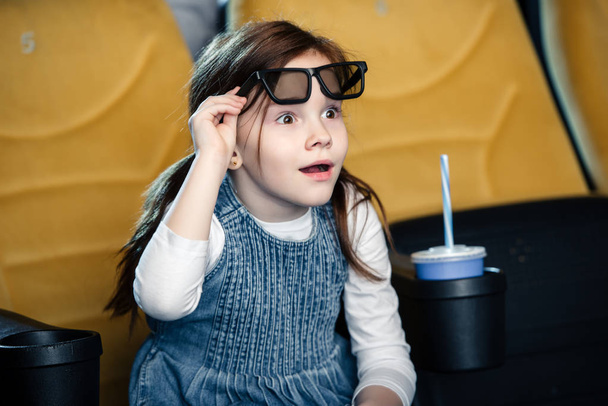 cute surprised child watching movie in cinema while sitting near paper cup - Foto, immagini