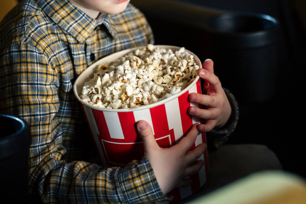 partial view of boy holding paper cup with popcorn while sitting in cinema - Fotoğraf, Görsel