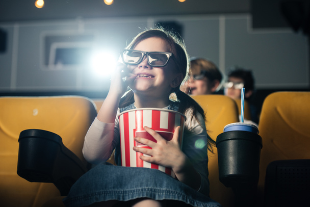 мила усміхнена дитина в 3d окулярах їсть попкорн і дивиться фільм в кіно
 - Фото, зображення