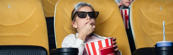panoramic shot of cute child in 3d glasses eating popcorn in cinema - Photo, Image