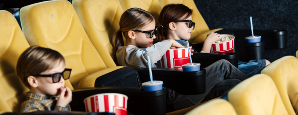 panoramic shot of children watching movie in 3d glasses and eating popcorn in cinema - 写真・画像