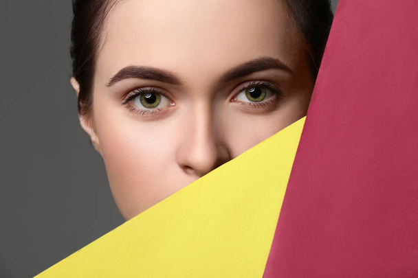 Young woman with beautiful eyebrows and color paper on grey background - Фото, изображение