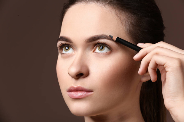 Young woman undergoing eyebrow correction procedure on color background - Photo, Image