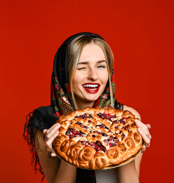 Portrait of a young beautiful blonde in headscarf holding a delicious homemade berry pie. - Foto, imagen