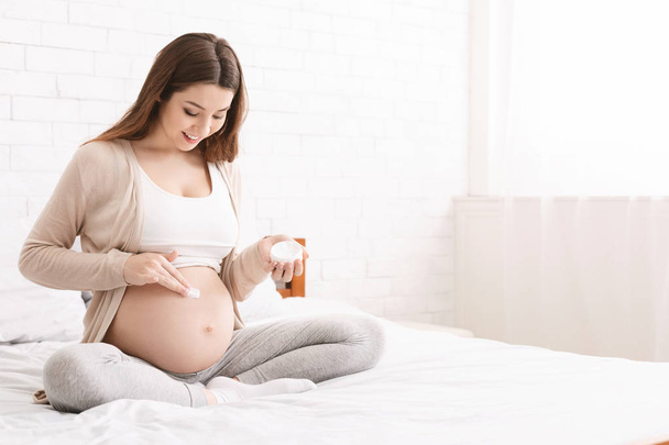 donna incinta che applica la crema smagliatura alla pancia - Foto, immagini