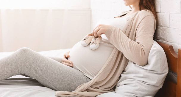 Small shoes for unborn baby on belly of pregnant woman - Foto, Imagem
