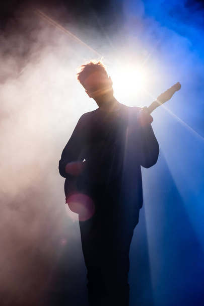 Κιθαρίστας παίζει κιθάρα στο σκοτάδι με μπλε οπίσθιου φωτισμού - Φωτογραφία, εικόνα