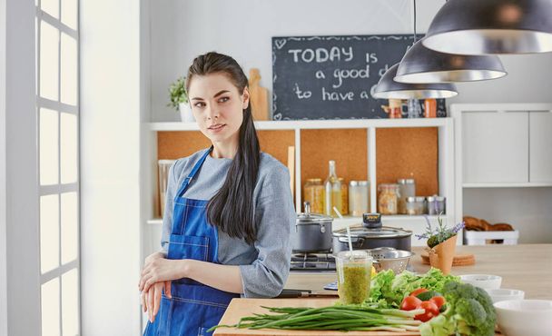 Happy young woman in kitchen with fresh vegetables on the table - Fotó, kép