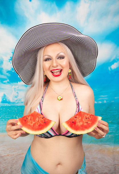 okouzlující baculatá blondýnka s velká prsa v plavkách stojí s kouskem melounu a těší se odpočinku a občerstvení - Fotografie, Obrázek