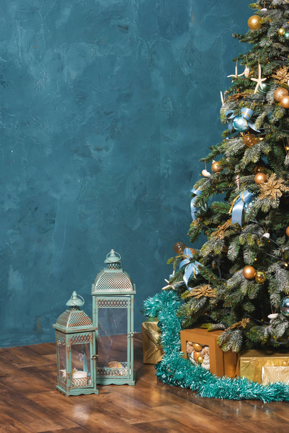 ゴールドとブルーカラーのクリスマスデコレーション。航海様式の新年の装飾。青の背景にクリスマスツリー上のヒトデ、リボンとボール。キャンドルと貝殻と東洋のスタイルで金属燭台. - 写真・画像