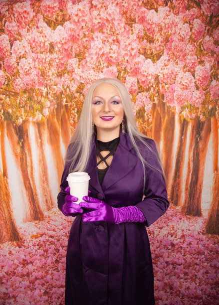 charmante femme blonde dodue dans un corset violet avec de longs gants tient une tasse de papier de café à emporter avec une marque de son baiser rouge à lèvres
  - Photo, image