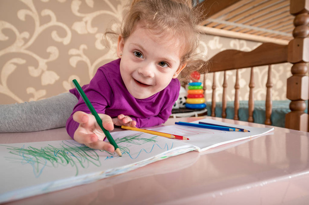 Cute cheerful child drawing using felt-tip pen while sitting at table - Photo, image