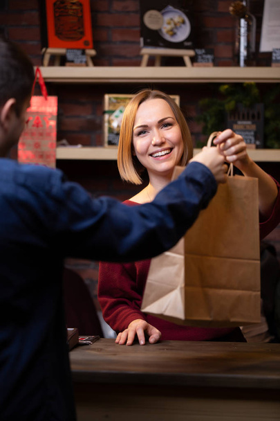Photo of happy seller blonde giving paper bag to man - Foto, Bild