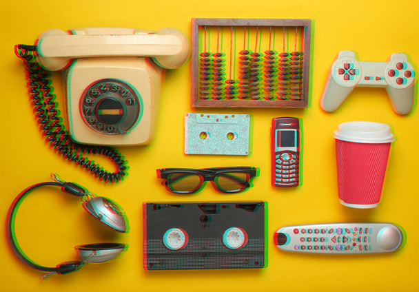 黄色の背景にレトロなオブジェクト。ロータリー電話、オーディオカセット、ビデオカセット、ゲームパッド、3d メガネ、テレビリモコン、ヘッドホン、プッシュボタン電話。過去のアナログメディア技術。フラットレイ - 写真・画像