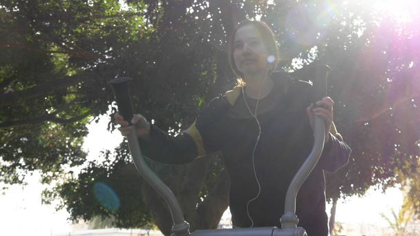 Беги с музыкой, молодая женщина использует уличный тренажер бега
 - Фото, изображение