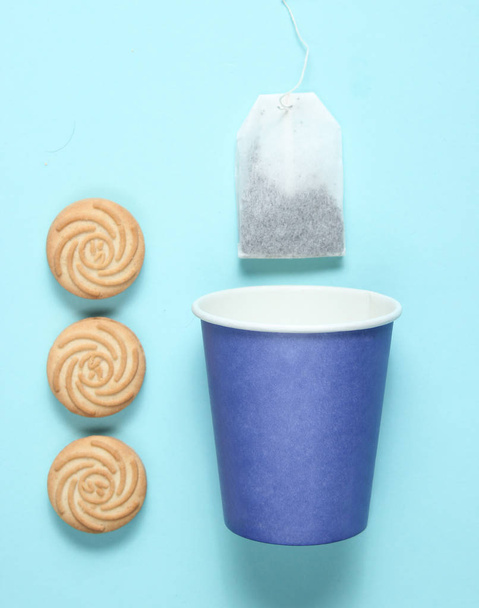 Taza de papel desechable vacía para té, bolsa de té, galletas sobre fondo pastel azul, vista superior, minimalis
 - Foto, imagen