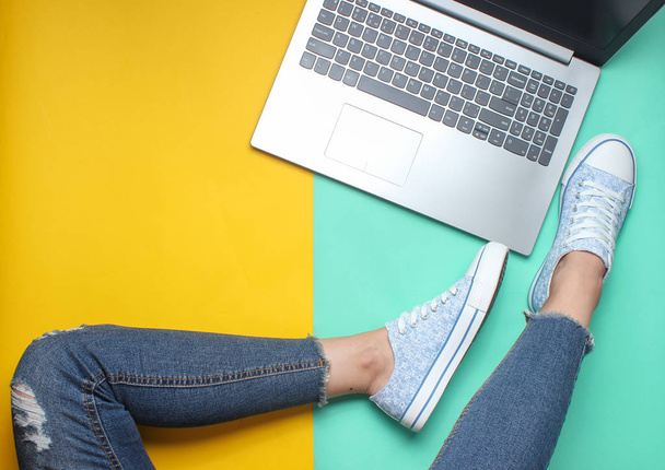 Dizüstü bilgisayar, kot pantolon ve spor ayakkabı renkli pastel arka plan, minimalizm, düz yatıyordu styl kadın bacaklar - Fotoğraf, Görsel