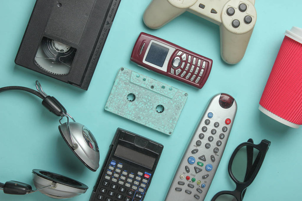 Ретро объекты на синем фоне. 3D очки, аудиокассеты, видеокассеты, геймпад, калькулятор, пульт от телевизора, наушники, кнопочный телефон. Аналоговые медиа технологии прошлого. Плоский лежал
 - Фото, изображение