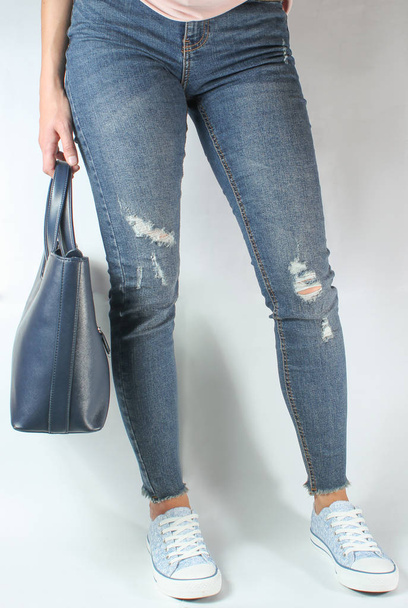 Женские ноги в джинсах и кроссовках, женщина, держащая кожаную сумку в руках на белой спине
 - Фото, изображение