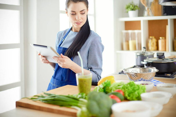 Young woman using a tablet computer to cook in her kitchen - Foto, imagen