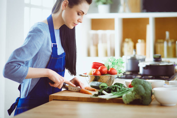 Young woman cutting vegetables in kitchen at home - Foto, immagini
