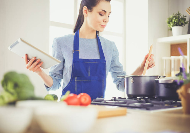 Young woman using a tablet computer to cook in her kitchen - Foto, imagen