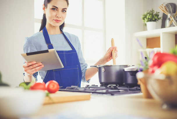 Young woman using a tablet computer to cook in her kitchen - Foto, immagini