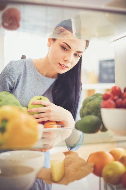 Smiling woman taking a fresh fruit out of the fridge, healthy food concept - Fotó, kép