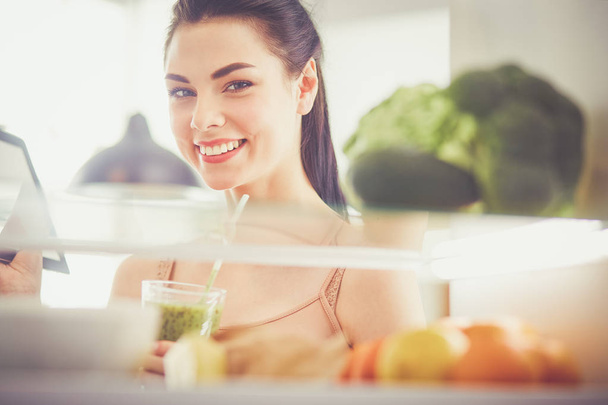 Smiling woman taking a fresh vegetable out of the fridge, healthy food concept - Fotó, kép