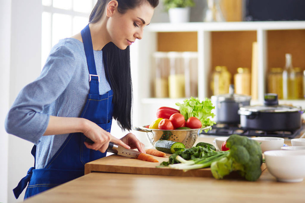 Young woman cutting vegetables in kitchen at home - Foto, imagen