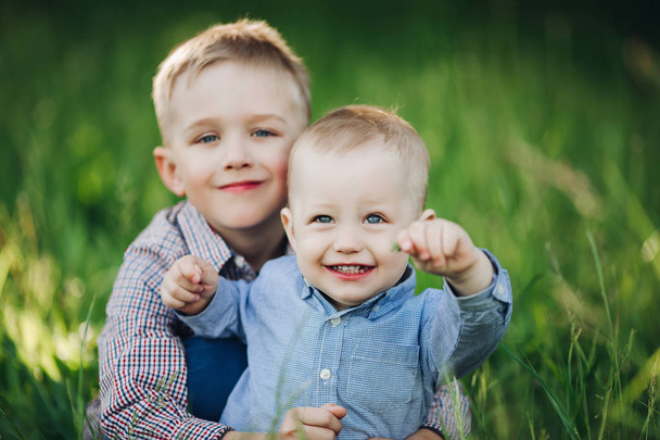 zwei kleine Brüder, die sich im Park umarmen und in die Kamera schauen. - Foto, Bild