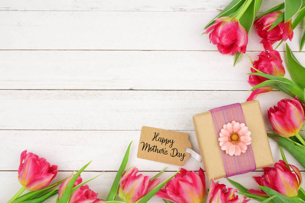 Hoek grens van roze bloemen met gelukkige Moederdag geschenk en tag tegen een rustieke witte houten achtergrond - Foto, afbeelding