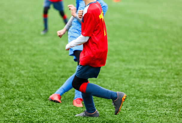 Young footballers dribble and kick football ball in game. Boys in red  blue sportswear running on soccer field. Training, active lifestyle, sport, children activity concept - Fotoğraf, Görsel