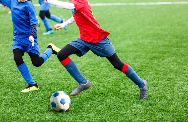 Jonge voetballers dribbelen en Kick Voetbal bal in het spel. Jongens in rood blauw sportkleding draait op voetbalveld. Training, actieve lifestyle, sport, kinderen activiteit concept - Foto, afbeelding