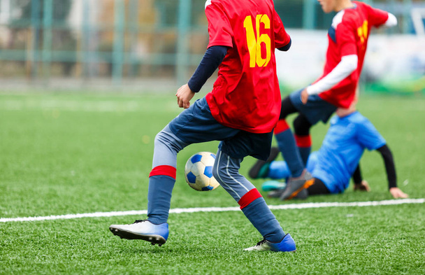 Fiatal labdarúgók csöpög és kick futball labda a játékban. Fiúk piros kék sportruházat futó focipályán. Képzés, aktív életmód, sport, gyermekaktivitási koncepció - Fotó, kép