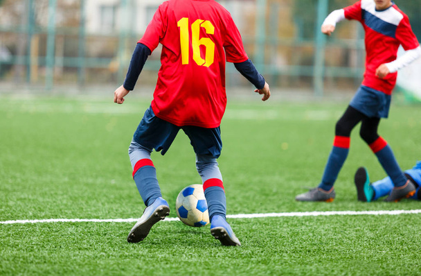 Młodzi piłkarze drybling i kick piłki nożnej w grze. Chłopcy w czerwonej niebieskiej odzieży sportowej biegną na boisku piłkarskim. Trening, aktywny styl życia, Sport, koncepcja aktywności dzieci - Zdjęcie, obraz