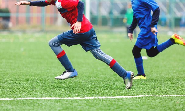 Young footballers dribble and kick football ball in game. Boys in red  blue sportswear running on soccer field. Training, active lifestyle, sport, children activity concept - Photo, Image