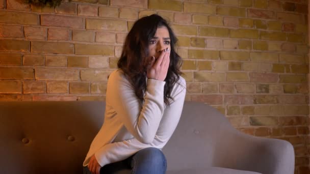 Portret van emotionele Kaukasische brunette vrouw zittend op sofa kijken thriller met zorg in gezellige huiselijke sfeer. - Video