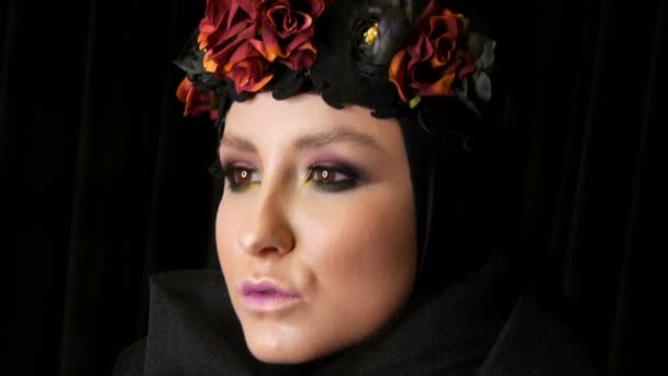 Profi-Model mit wunderschönem Make-up posiert mit schwarzer Mütze und Kranz auf dem Kopf vor der Kamera auf schwarzem Hintergrund im Bild einer schwarzen Witwe. Mode im Trend - Filmmaterial, Video