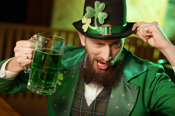 Dark-haired bearded young man in a leprechaun hat with shamrock having fun - Photo, image