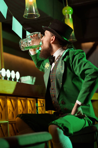 Dark-haired bearded young man in a leprechaun costume having good time in the pub - Фото, зображення