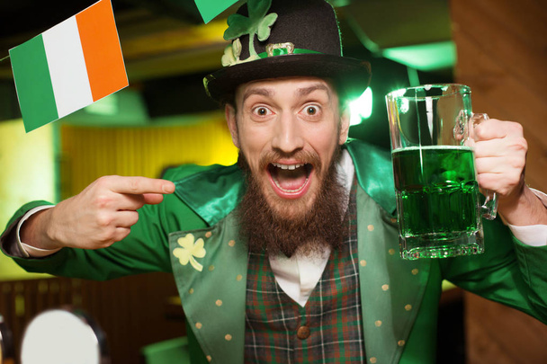 Dark-haired bearded young man in a leprechaun costume having great time in the pub - Foto, imagen