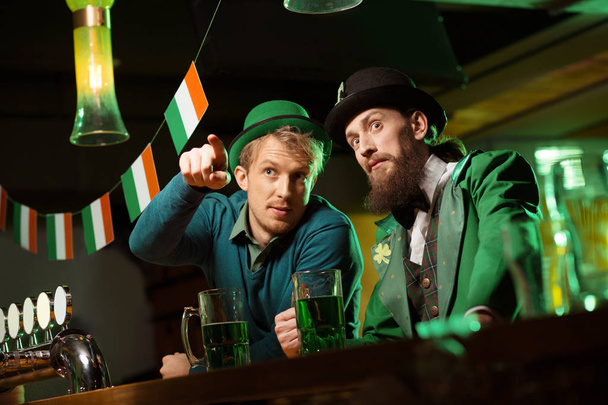 Fair-haired young man in a green hat showing something to his bearded friend - Photo, Image