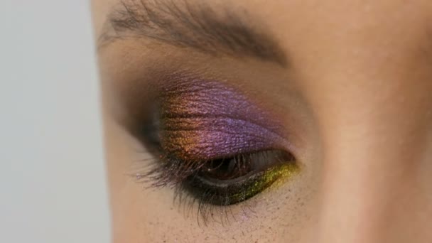 Modieuze multi-gekleurde oogschaduw kameleon met geel paars grijs zilver kleur op het ooglid van mooi meisje model met bruine ogen. Professionele cosmetische make-up. Close-up van oog - Video