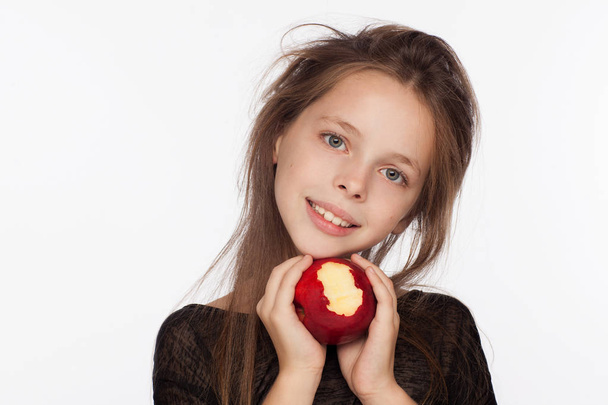 Beautiful emotional eight-year-old girl with an apple. Photo session in the studio. The girl is wearing a black blouse - Foto, imagen